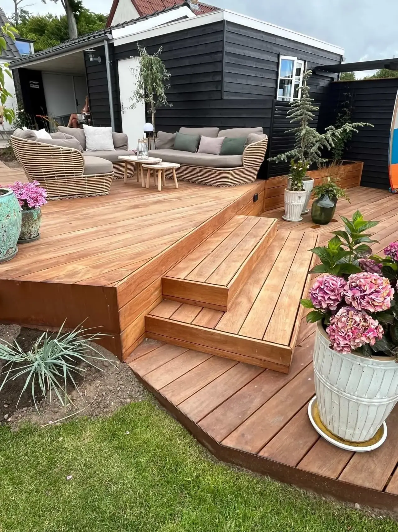 Hyggelig træterrasse med sofaer og blomsterkrukker